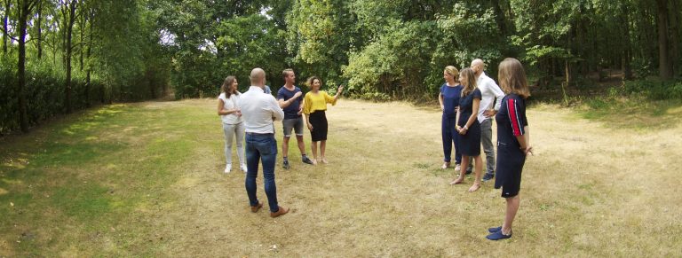Team staat in een kring in een bosweide tijdens een Gesprek op voeten